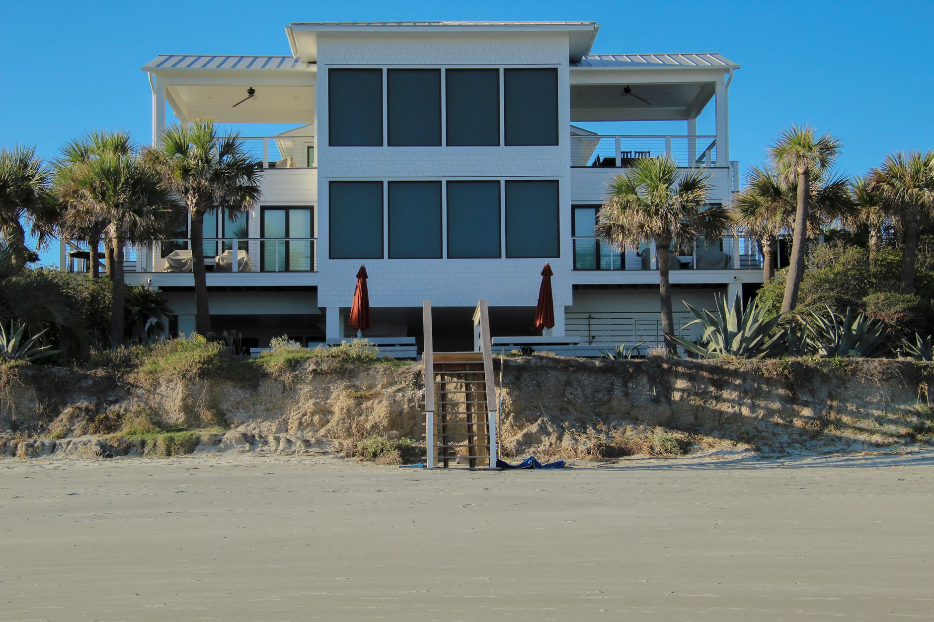 A modern beachfront house with palm trees under a clear blue sky.