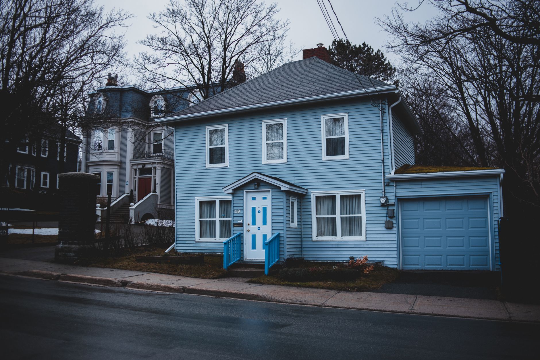 Exterior of small residential house trimmed with light blue wooden panels with white door and adjoin garage